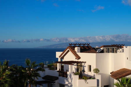 White apartment with a balcony, palm trees and views of the Atlantic ocean and La Gomera island. Against the blue sky.の写真素材