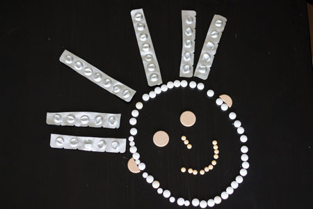 A funny face made out of pills of different colors and sizes with hair made out of empty blisters on...