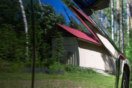 A white house with a tiled roof, trees and sky reflected in the door of a black car ...の写真素材