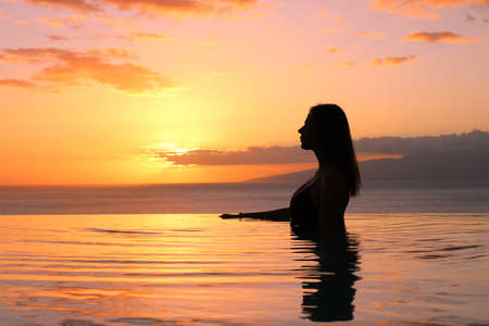 A girl with shoulder-length hair, in a bathing suit stands sideways in the pool and watching the sunset.hotel Las Terrazas de Abama.の写真素材