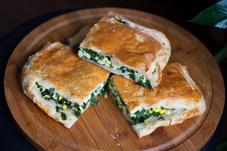 Sliced homemade layer cake with green onion and egg on a round wooden Board on a black background.の写真素材