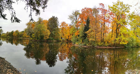 Trees with colorful leaves growing on the shore of the pond and reflected in its waters in the park on the Elagin Island of St. Petersburg.の写真素材