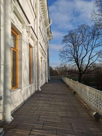 A tile road along the Elaginoostrovsky Palace with a beautiful fence against a background of leafless trees and a blue sky with clouds in the autumn park of St. Petersburg.の写真素材