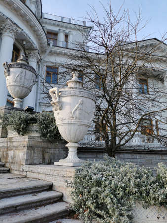 Saint-Petersburg. Russia. 09/11/2021. Stone vases with flower beds with plants whose leaves are in frost against the background of the Elaginoostrovsky Palace and the blue sky in the autumn park of St. Petersburg.のeditorial素材