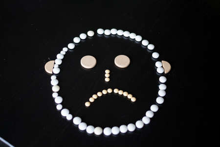 A sad face made out of pills of different colors and sizes on a black background.の写真素材