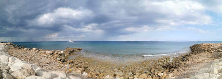 Protaras. Famagusta area. Cyprus. panorama. The stone coast of the Mediterranean Sea, a white ship in the sea and the largest sailing yacht in the world against a dramatic sky.の写真素材
