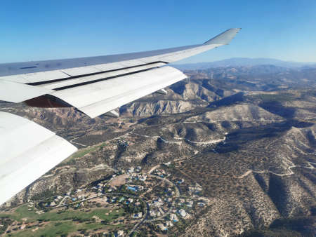 View from the porthole on the gray wing of the plane with the flaps extended, landing in Cyprus, in the morning over the beautiful mountains and settlementsの写真素材