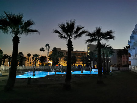 Protaras. Cyprus. Sunrise in Cyprus. A swimming pool surrounded by sun loungers and parasols surrounded by palm trees against a blue and yellow skyのeditorial素材
