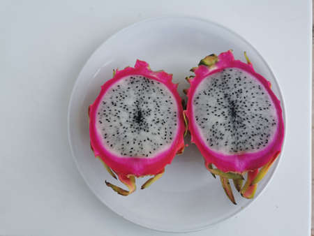 Pink outside and white inside pitahaya (pitahaya or dragon's eye) - the fruit of Hylocereus cacti, cut in half, lying on a white plate.の写真素材