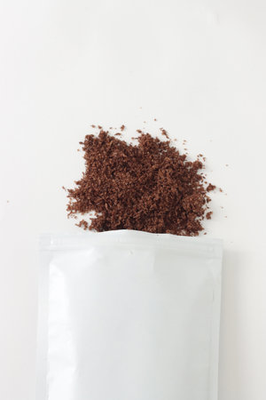 scattered brown texture scrub with cocoa coconut and coffee from pack on white background. spa and home care concept, beauty procedures, vertical photoの写真素材