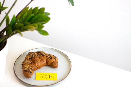 chocolate croissant on plate with kcal label. Concept counting calories, food control, Intuitive eating, breakfast, copyspaceの写真素材