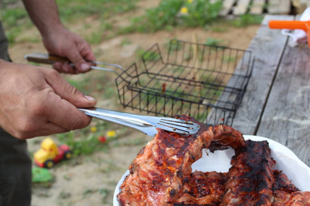 a man holds meat on ribs with cooking tongs at a picnicの写真素材