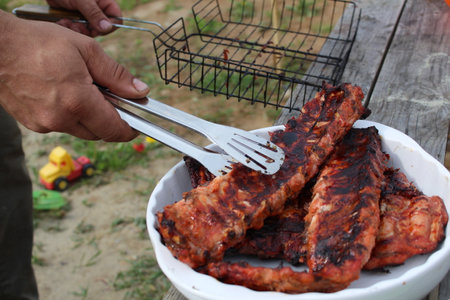 a man holds meat on ribs with cooking tongs at a picnicの写真素材