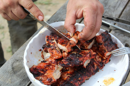 a man cuts pork ribs on the grill with a knife during a picnicの写真素材