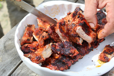 a man cuts pork ribs on the grill with a knife during a picnicの写真素材