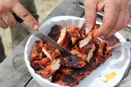 a man cuts pork ribs on the grill with a knife during a picnicの写真素材