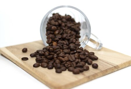 Scattered coffee beans from the glass cup on the wooden plank.の写真素材
