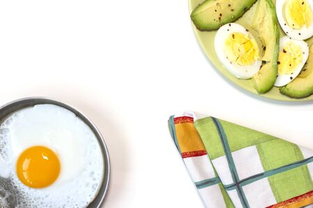 Green plate with boiled egg and avocado seasoned with salt and paper. One fried egg on the little pan. White background. Copy space. Place for text and design. Top view. Flat lay.の写真素材
