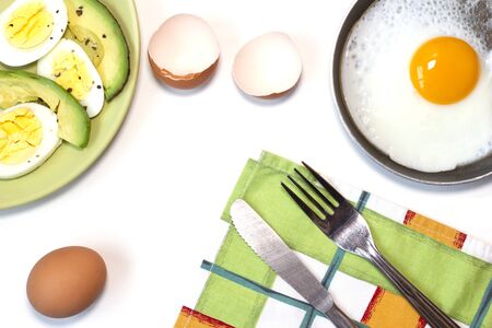 One fried egg on the little pan, avocado, boiled egg, dish towel, fork and knife. White background. Top view. Flat lay. Copy space. Place for text and designの写真素材
