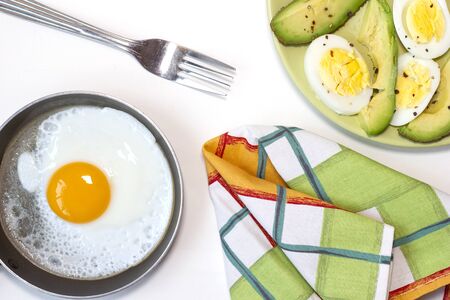 Green plate with boiled egg and avocado seasoned with salt and paper. One fried egg on the little pan. White background. Top view. Flat lay.の写真素材