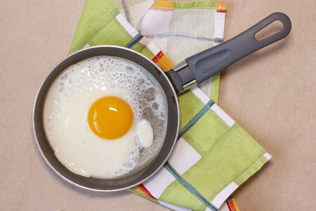 One fried egg on the little pan, dish towel. Craft brown background. Top view. Flat lay.の写真素材