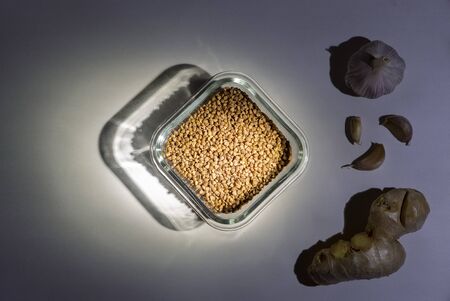 Buckwheat in the glass container, ginger and garlic on the dark background.Play of light. Flat lay