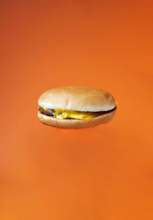One cheeseburger in the air. Bright orange background. Copy space. Place for text and design. Fast food idea. Food delivery conceptの写真素材