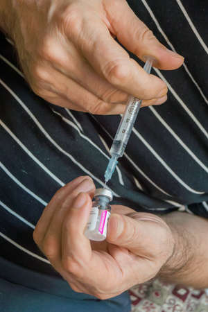 Man picking solution in a syringe to make himself a prickの写真素材