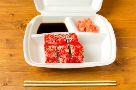 Ready-to-delivery of california roll, soy sauce and ginger lie in a container next to unpacked chopsticks.の写真素材