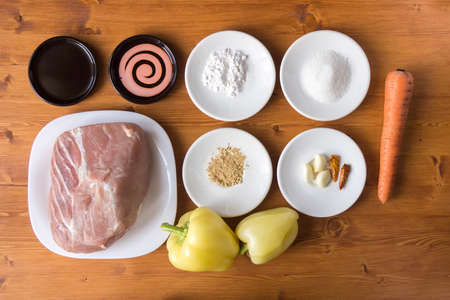Pork, vegetables, condiments, spices for cooking dishes lie in a pot on a wooden table.の写真素材