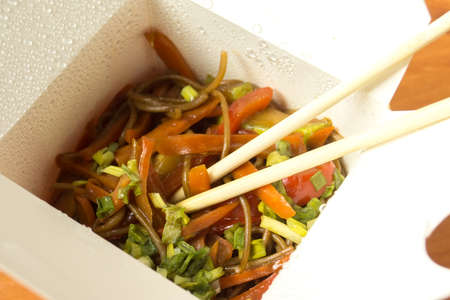 Open box with noodles, vegetables, sauce and chopsticks.の写真素材