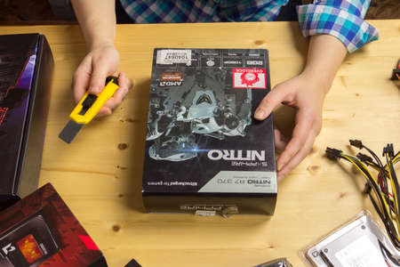 TVER, RUSSIA - NOVEMBER, 21, 2016: Woman unpacks using stationery knife a new video card to your computer at a wooden table.のeditorial素材