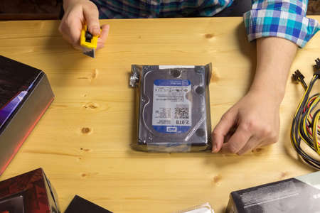 TVER, RUSSIA - NOVEMBER, 21, 2016:  Woman unpacks using stationery knife new hard drive to the computer at a wooden table.のeditorial素材