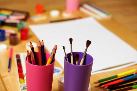 Brushes and colored pencils are in the Cup on the background of a blank sheet of paper and paints.の写真素材