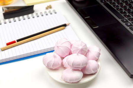 A full plate of pink marshmallows in the background of laptop, notebook, pencils.の写真素材