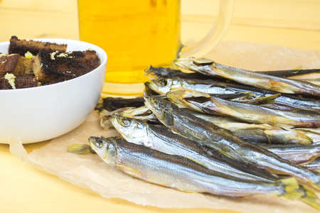 Dried fish near the garlic croutons on the background of a glass mug of light beer.