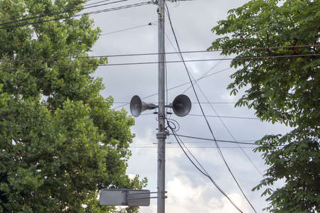 Broadcasting loudspeakers on a pole in the city between the trees