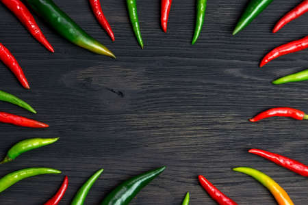Red and green hot peppers on a black wooden table laid out in a circle