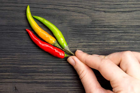 Green, orange and red hot peppers in hand on a wooden table