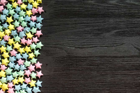Beautiful background with light multi-colored paper stars on a black wooden surfaceの写真素材
