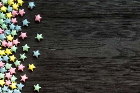Beautiful background with light multi-colored paper stars on a black wooden surfaceの写真素材