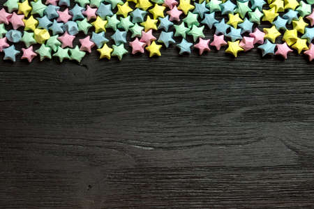 Beautiful background with light multi-colored paper stars on a black wooden surfaceの写真素材