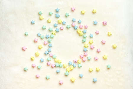Beautiful background with light multi-colored paper stars laid out in a circle on a beige plaidの写真素材