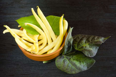 Yellow bean pods (haricot) in a clay bowl on a wooden table, legumes harvest