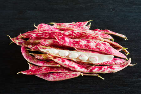 Pink spotty bean pods (Phaseolus) on a wooden black table. Harvest season