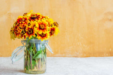 A bouquet of orange-red zinnias in a jar on a rustic background.の写真素材