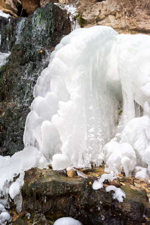 Ice frozen on the edge of the waterfall in a frosty winter. Cold day by the riverの写真素材