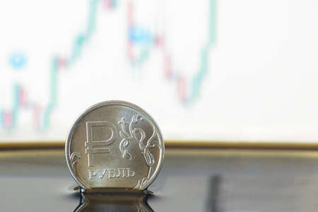 A coin with a sign and an inscription ruble in crude oil against the background of a price change chartの写真素材