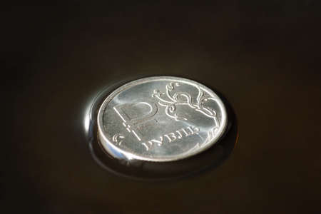 Coin with ruble sign on crude oil surface. Sale of natural resources. Inscription - rubleの写真素材