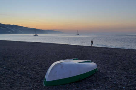 boat upside down on the beach of Castell de Ferro during a sunrise. Fisherman silhouette, boats in the sea and mountainsの写真素材